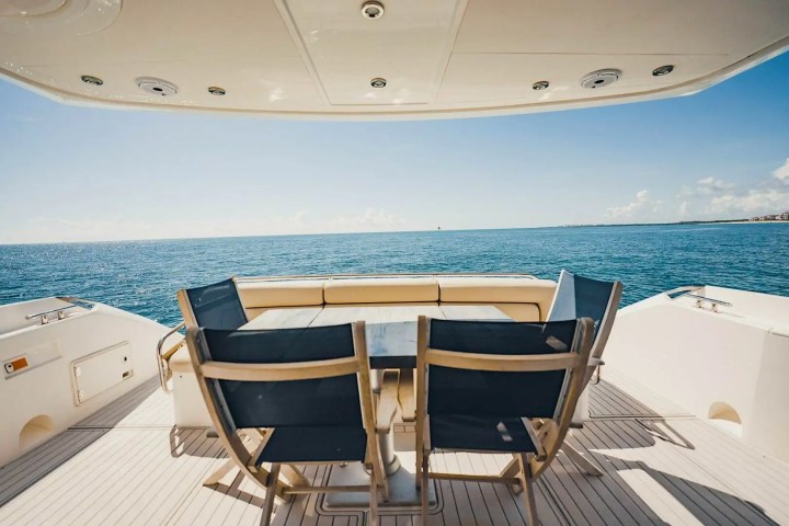 Yacht deck with chairs and table overlooking the ocean under a sunny sky.
