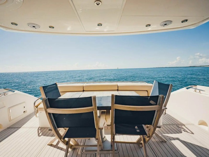 Yacht deck with chairs and table overlooking the ocean under a sunny sky.