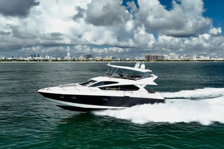 Luxury yacht cruising on the ocean with a cityscape and clouds in the background.
