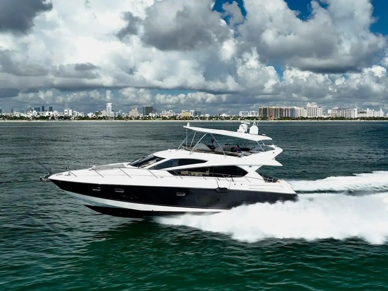 Luxury yacht cruising on the ocean with a cityscape and clouds in the background.