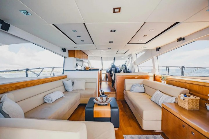 Luxurious yacht interior with cream sofas, wood accents, and large windows showing ocean view.