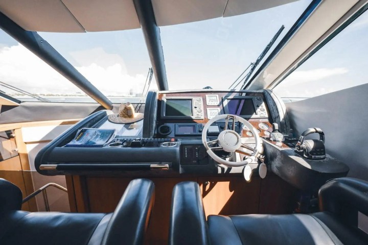 Interior of a yacht cockpit with steering wheel, control panels, and leather seats.