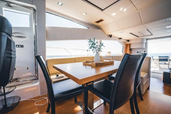 Interior of a boat with a wooden table, black chairs, and a window view of the ocean.
