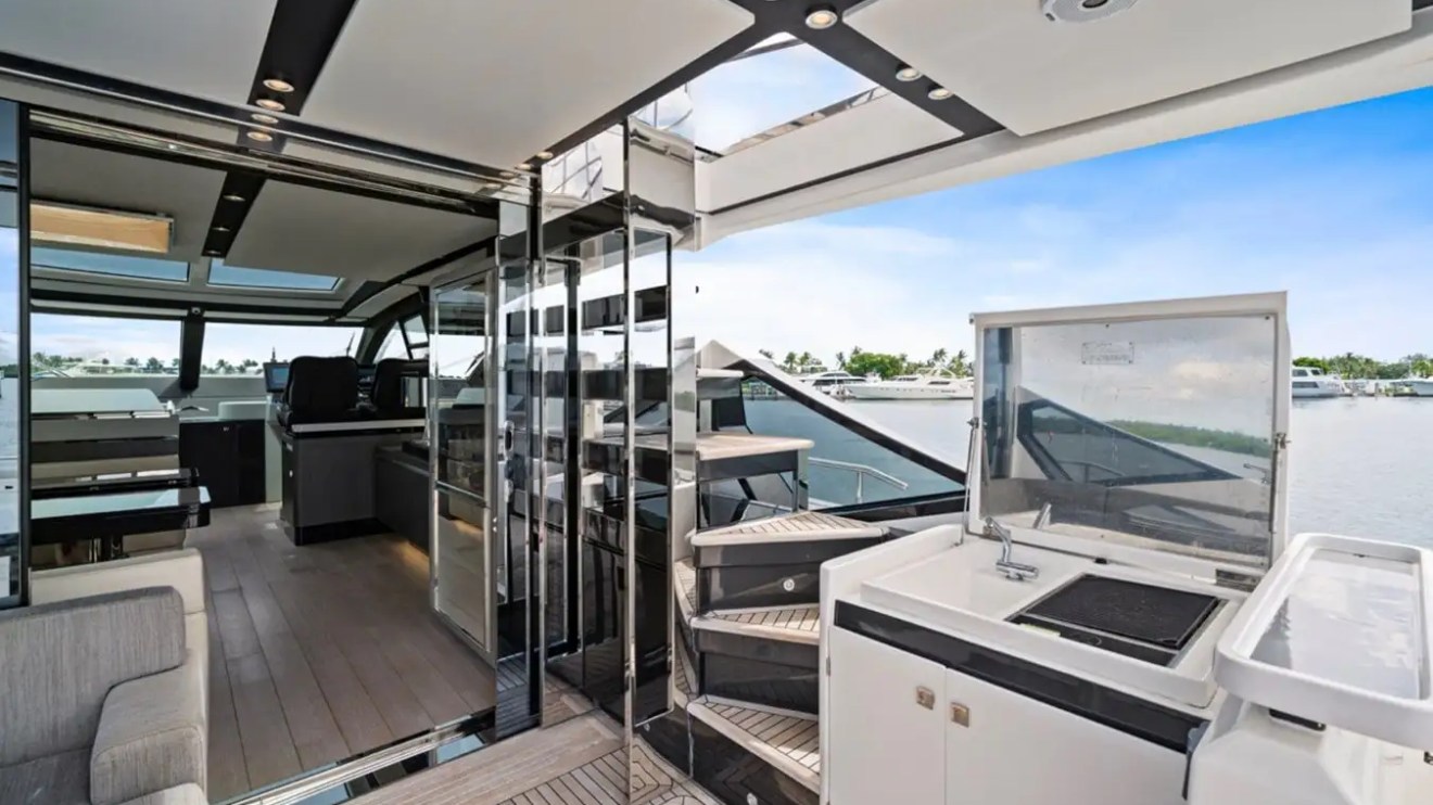 Modern yacht interior with seating, kitchenette, and stairs to upper deck, overlooking water.