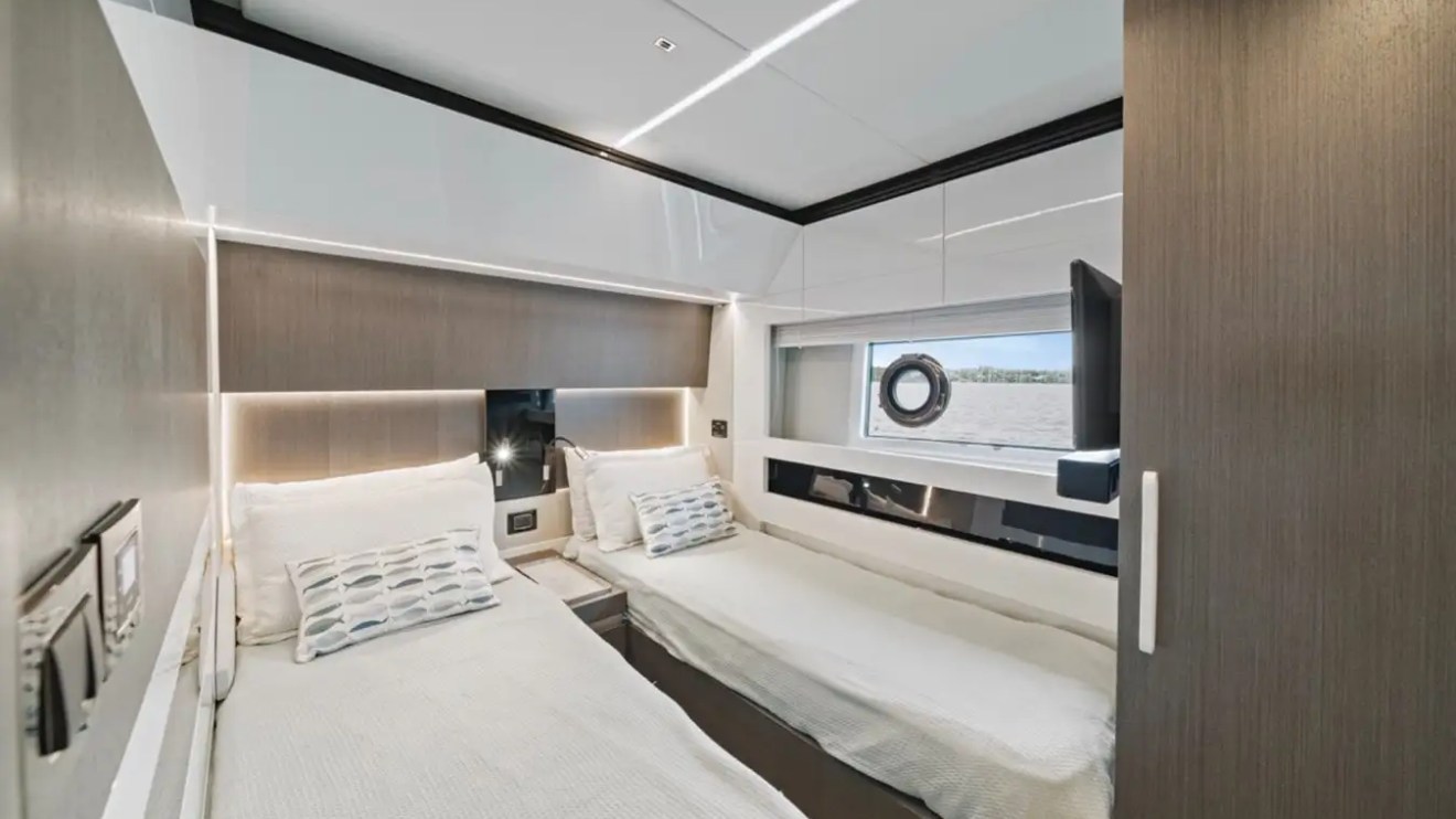 Modern boat cabin with two twin beds, a circular window, and a wall-mounted TV.