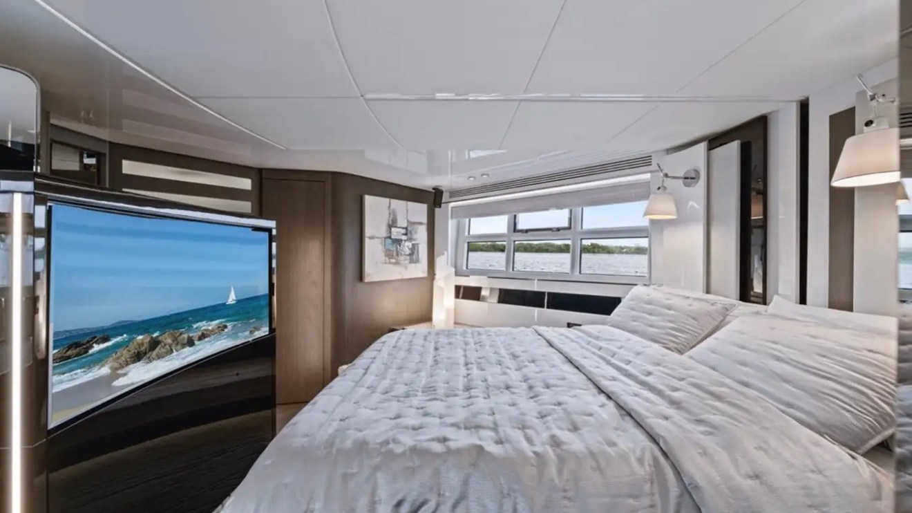Luxury yacht bedroom with large bed, TV, and scenic window view.