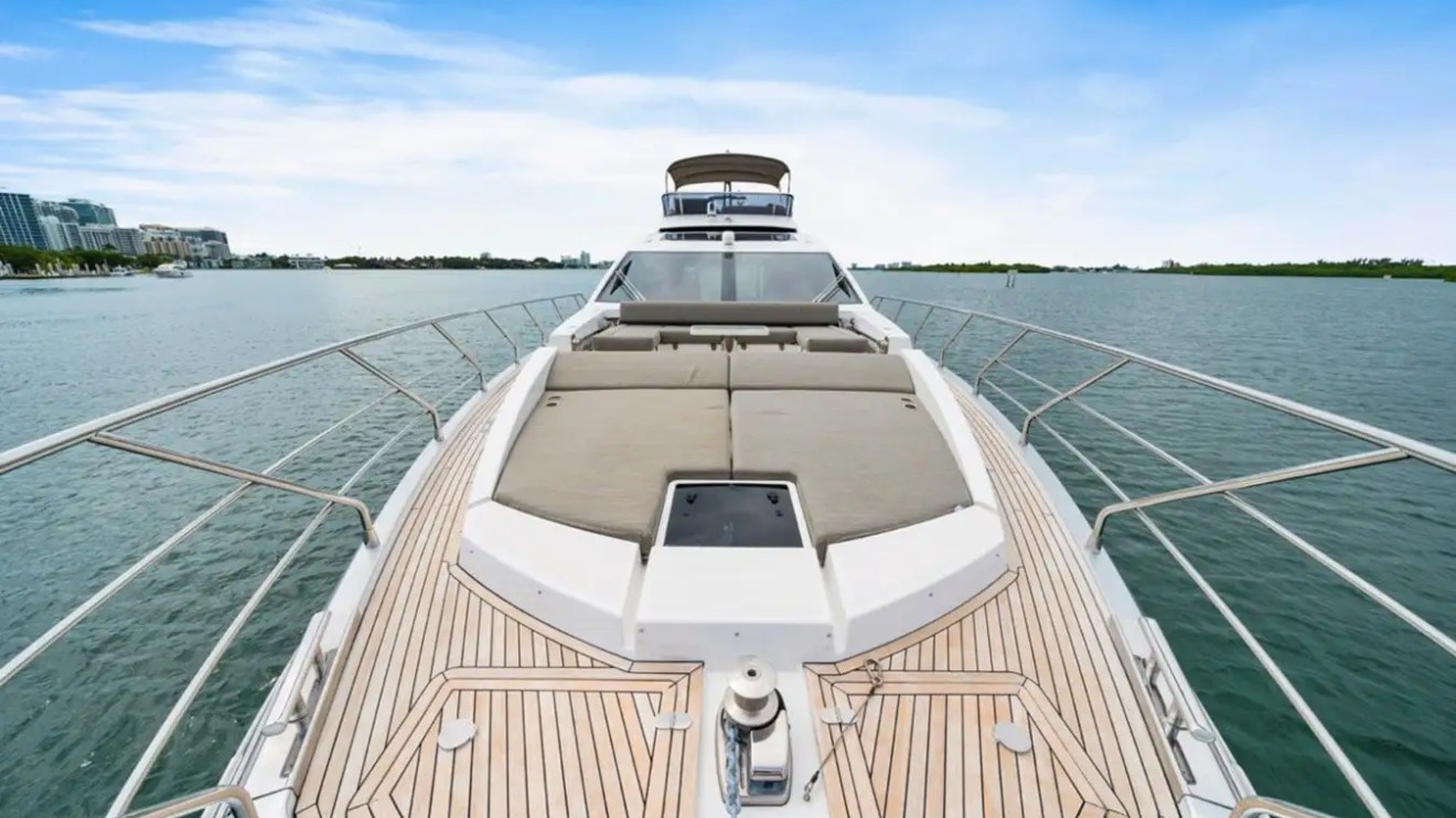 View from the bow of a yacht with cushioned seating, ocean and city skyline in background.