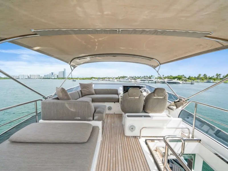 Luxury yacht deck with seating under a canopy, overlooking calm waters and distant skyline.