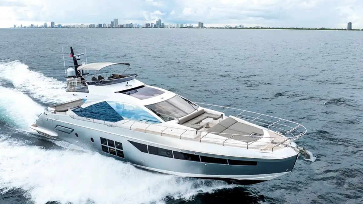 Luxury yacht cruising on a calm ocean with city skyline in the background.