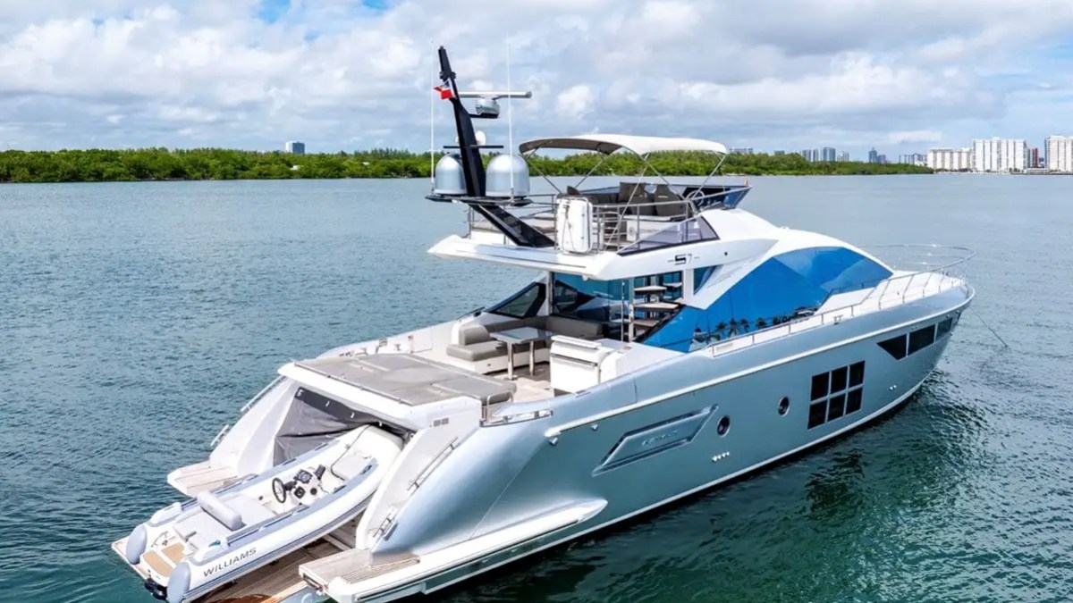 Luxury yacht on water with jet ski at the back, city skyline in the distance.