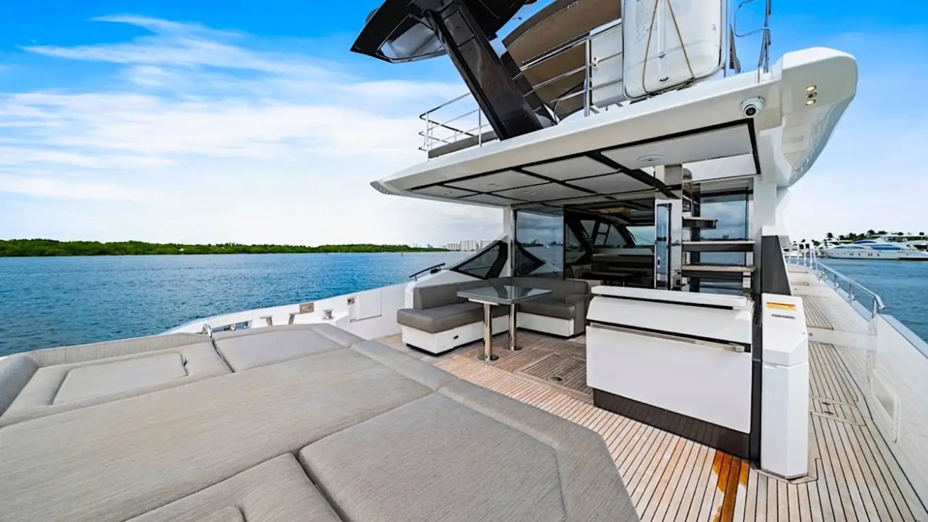 Luxury yacht deck with seating, table, and canopy, overlooking calm blue water and clear sky.