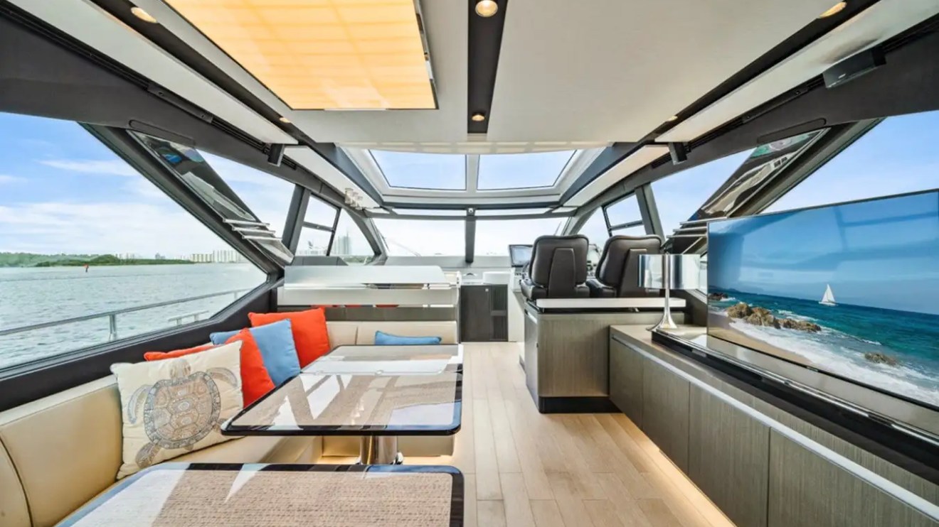 Luxurious yacht interior with tables, cushioned seats, and widescreen TV showing a beach scene.