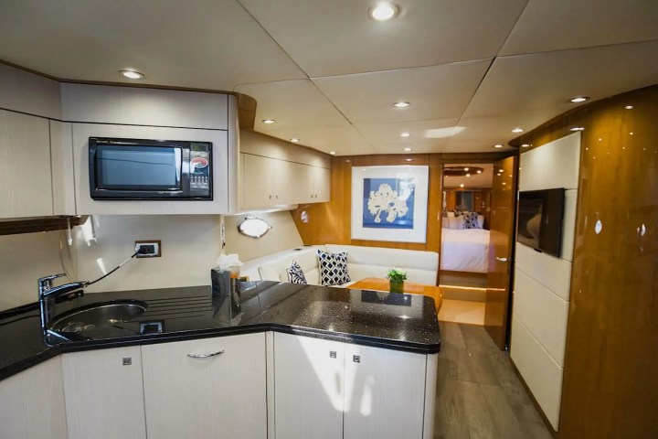 Modern yacht interior with kitchenette, TV, seating area, and bedroom in the background.