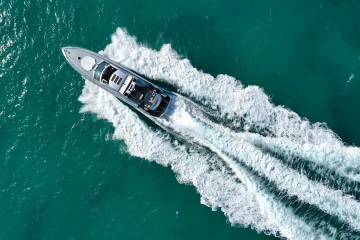 Aerial view of a yacht cruising through turquoise water, leaving a white wake behind.