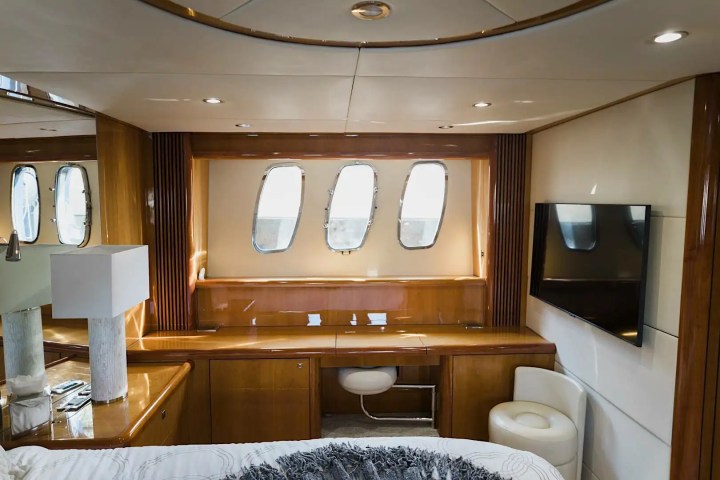 Luxurious yacht cabin with wood paneling, windows, TV, lamp, and white bedding.