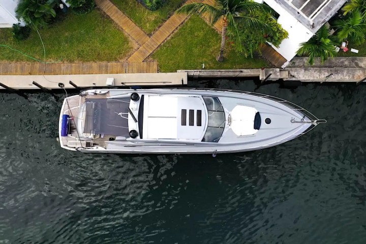 Aerial view of a yacht docked beside a grassy area with palm trees and a walkway.
