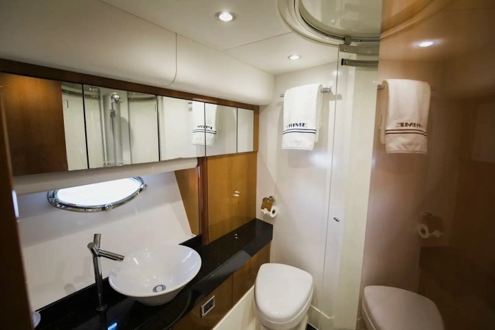 Modern yacht bathroom with sink, mirror, toilet, shower, and towels.