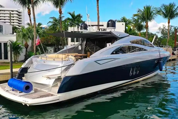 Luxury yacht docked by palm trees, with a rolled mat on deck.
