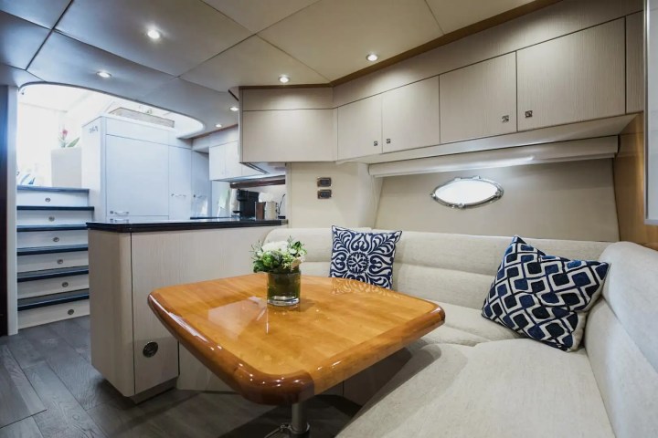 Boat cabin interior with table, sofa, and blue patterned cushions, featuring a small vase with flowers.