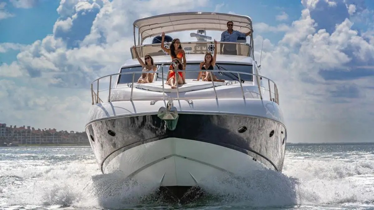 A yacht on the ocean with four people relaxing on the deck under a partly cloudy sky.