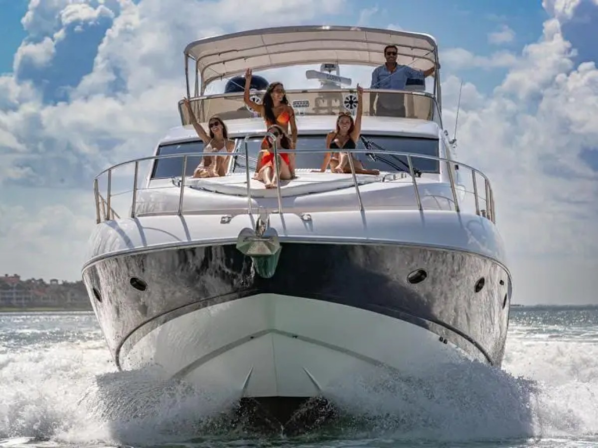 A yacht on the ocean with four people relaxing on the deck under a partly cloudy sky.
