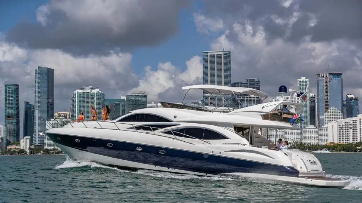 Luxury yacht cruising with city skyline in the background and people on deck.