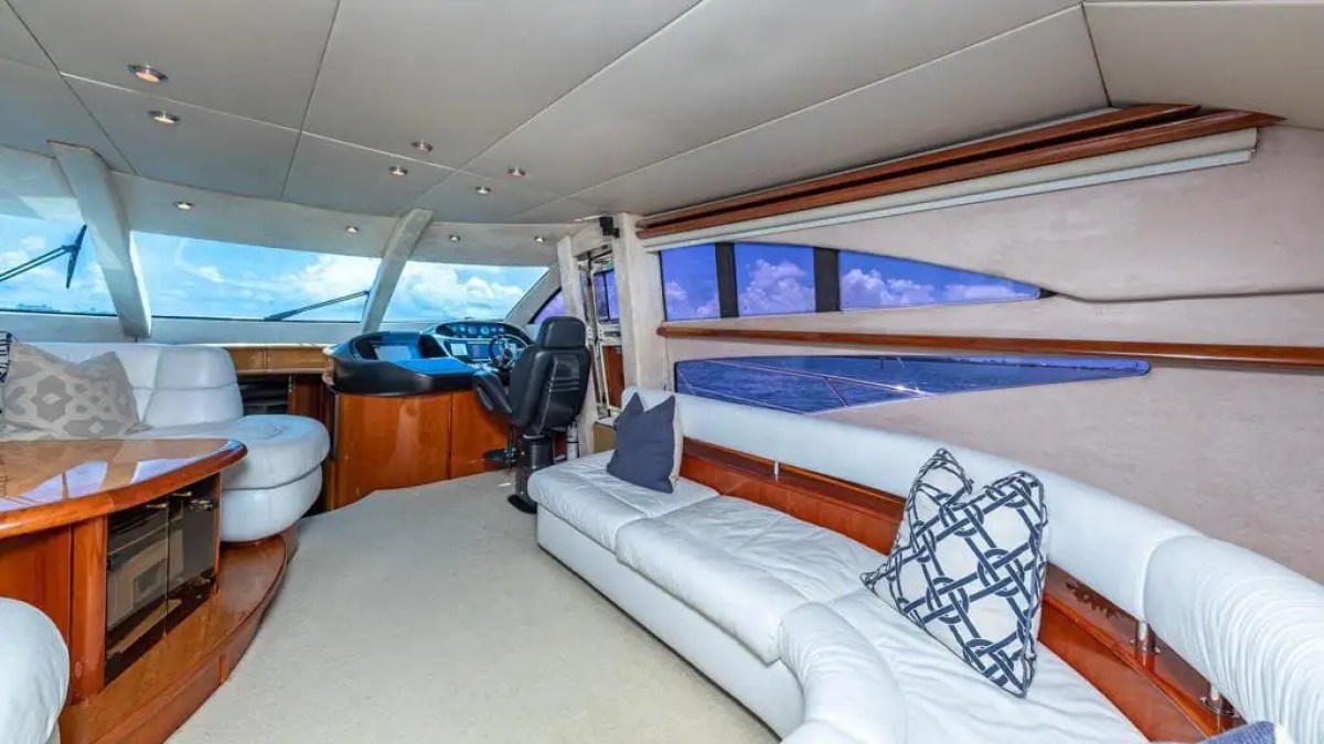 Luxurious yacht interior with white sofas, helm, and large windows showing sea view.