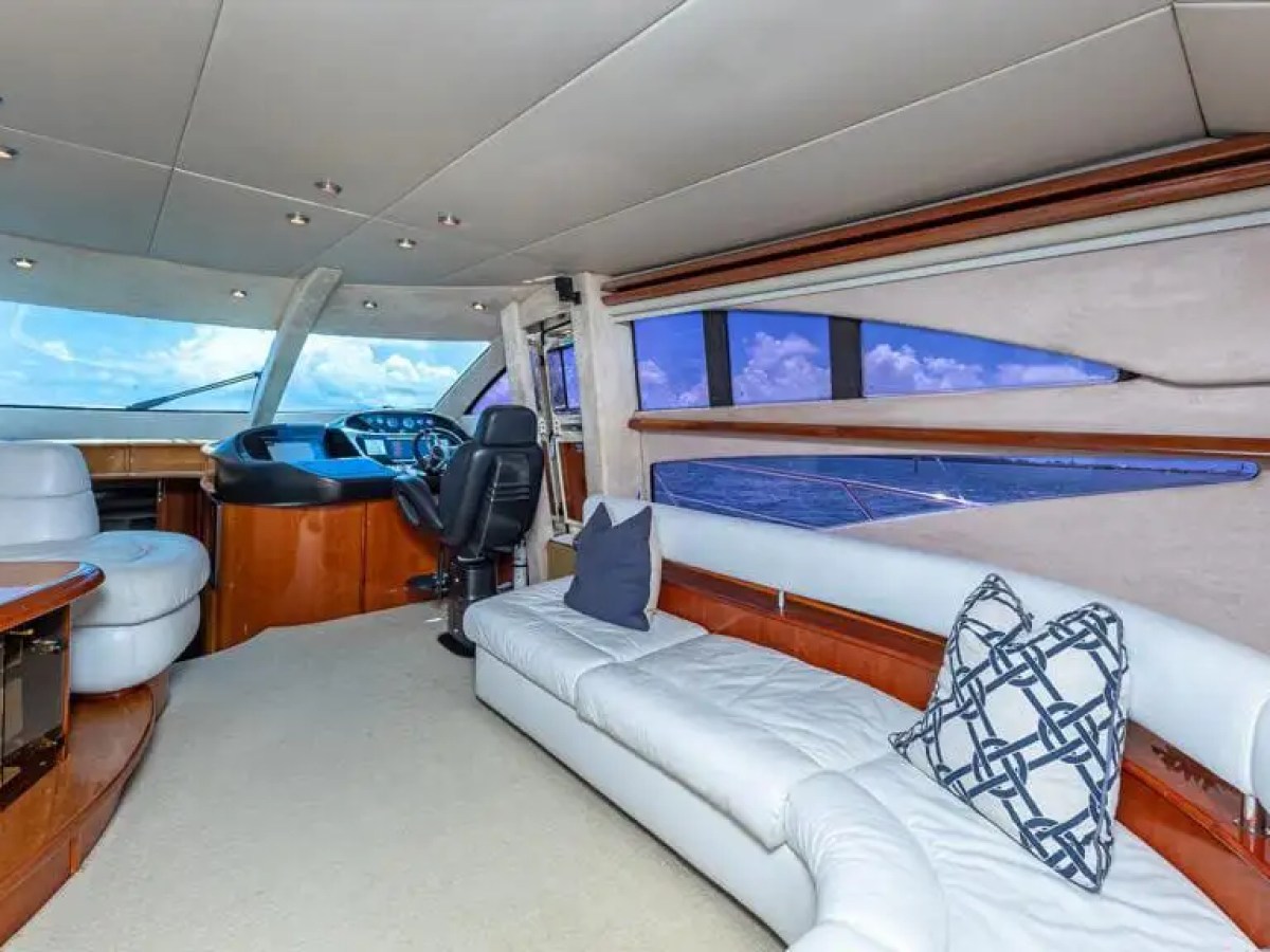 Luxurious yacht interior with white sofas, helm, and large windows showing sea view.
