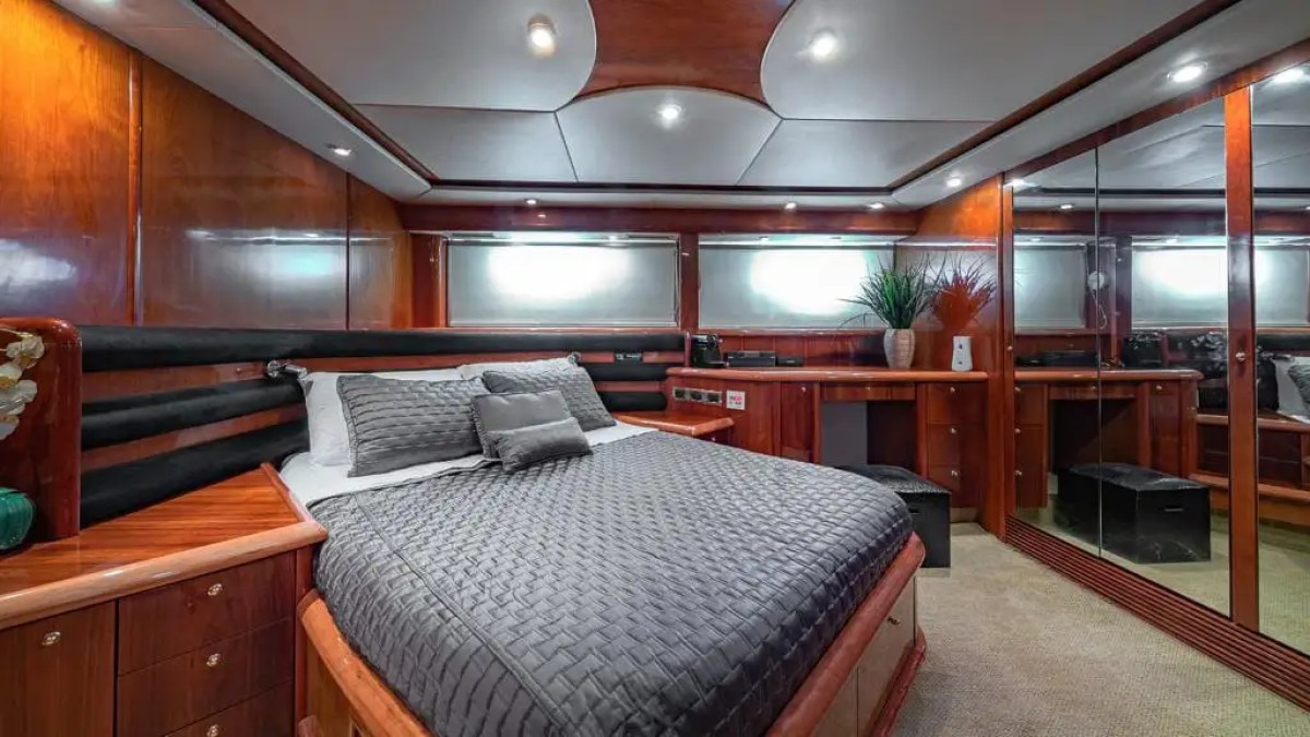 Luxurious yacht bedroom with wooden panels, grey bedding, and a mirrored wall.
