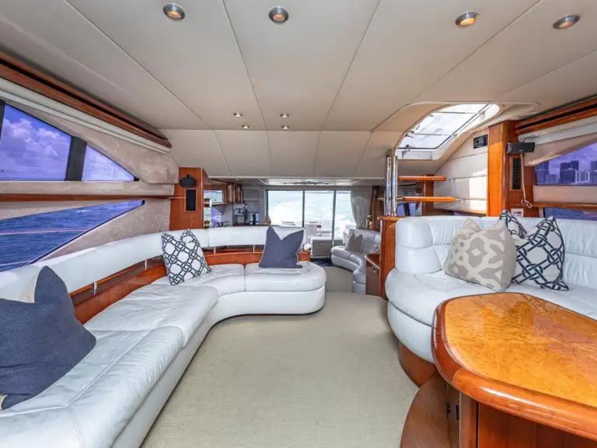 Luxurious yacht interior with white leather sofas, wooden accents, and city skyline view through windows.