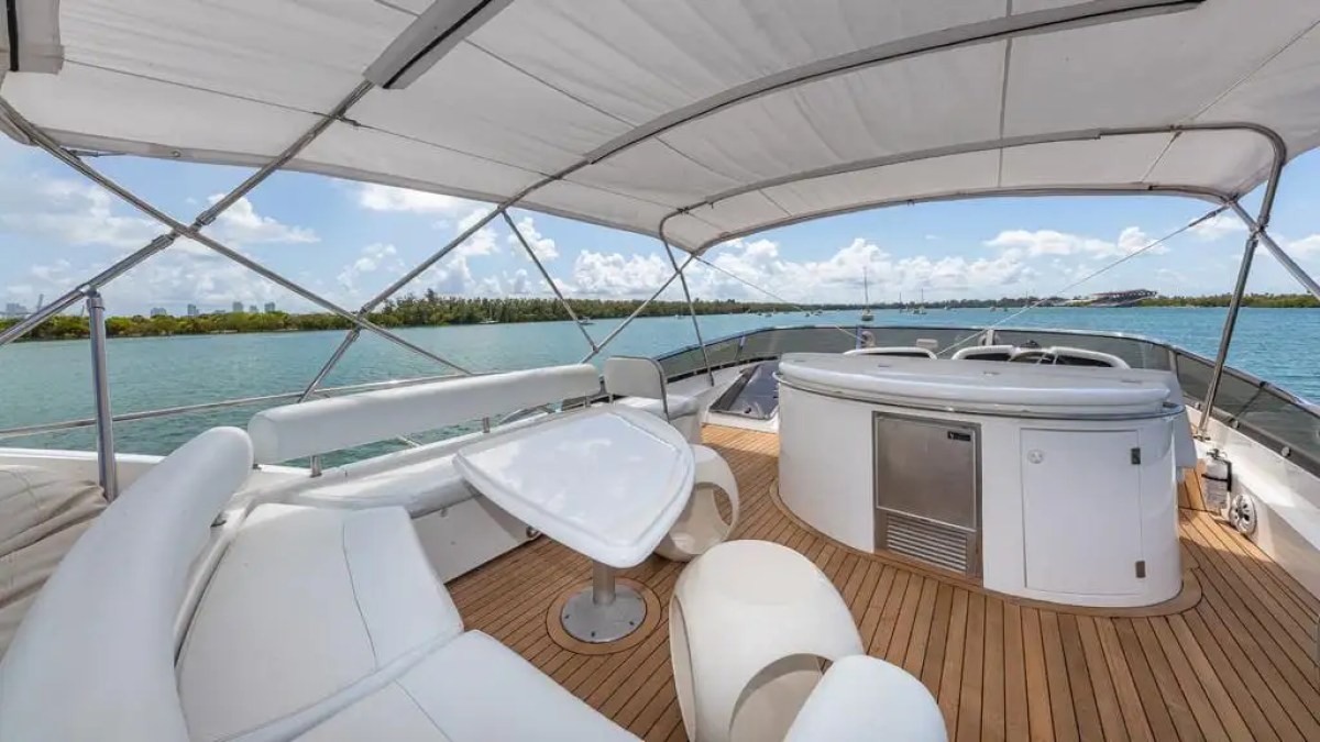 Luxury yacht deck with white seating, table, and bar under canopy, overlooking water.
