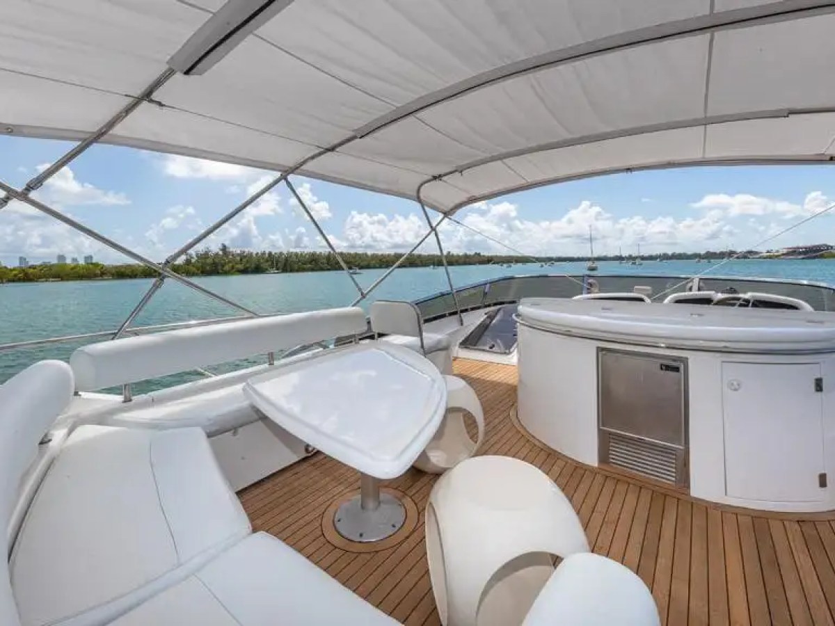 Luxury yacht deck with white seating, table, and bar under canopy, overlooking water.
