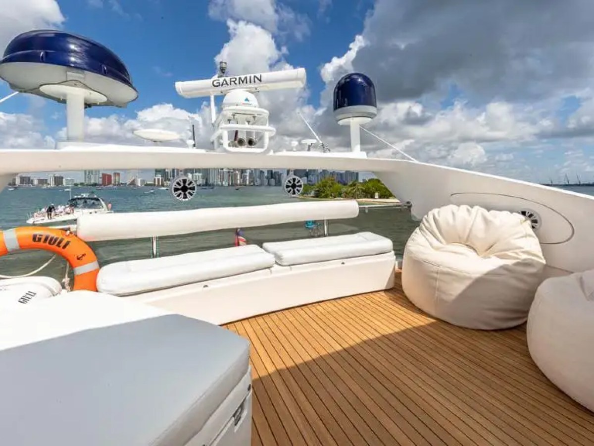 Boat deck with white seating, bean bags, and a lifebuoy, overlooking a city skyline and cloudy sky.