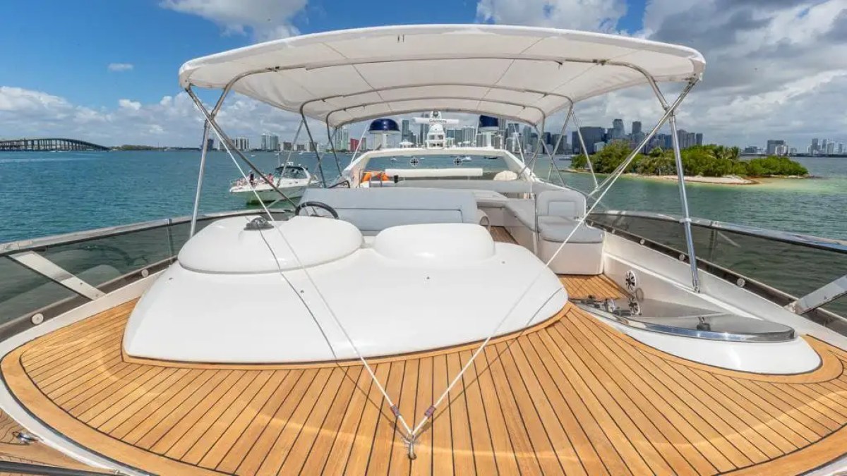 Luxury yacht deck with wooden flooring and canopy, city skyline and water in the background.