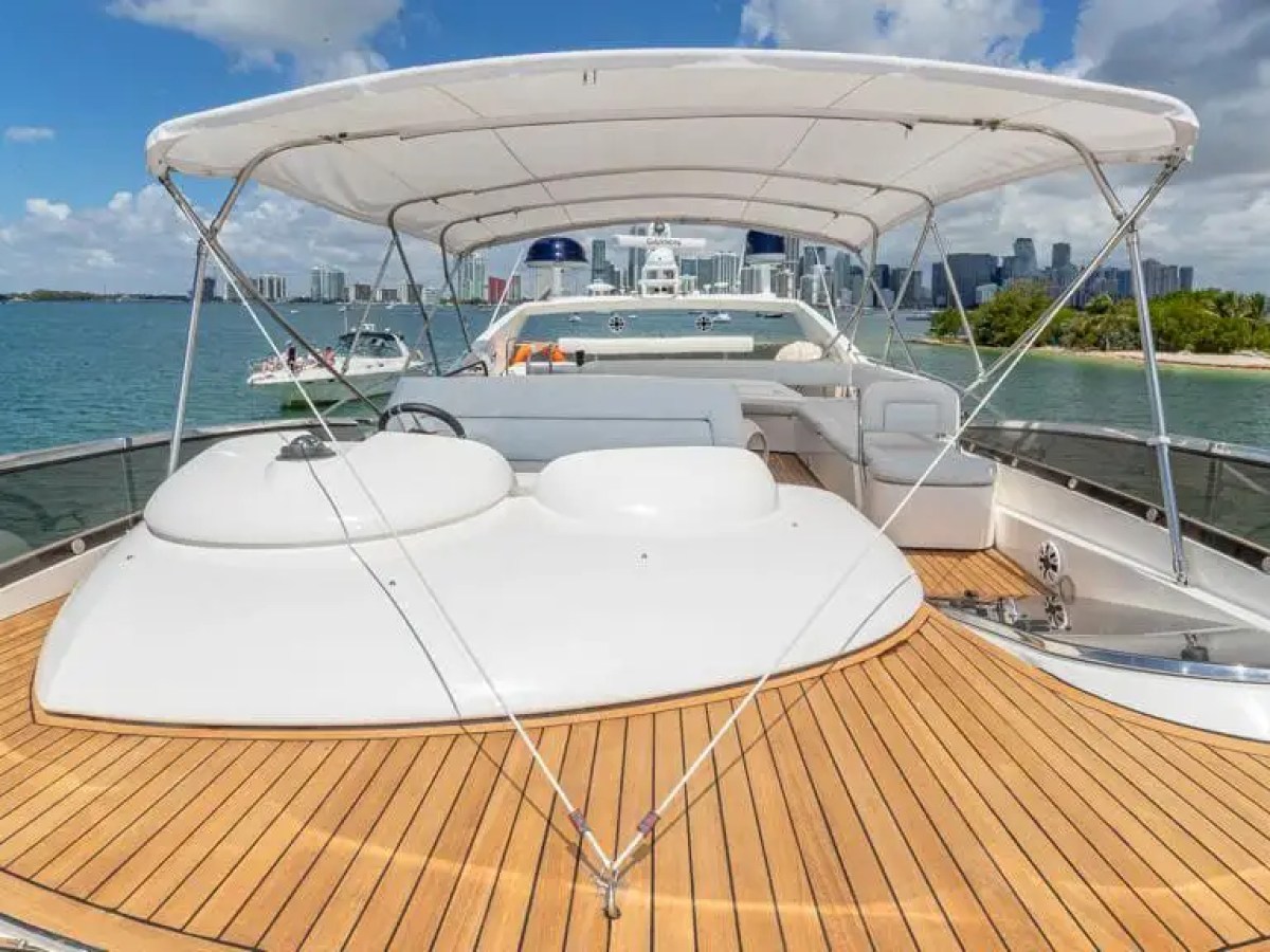 Luxury yacht deck with wooden flooring and canopy, city skyline and water in the background.