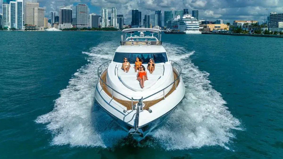 Luxury yacht with people sunbathing on deck, city skyline in background.