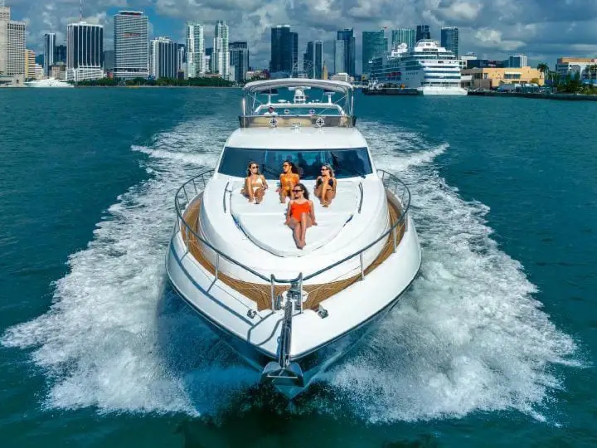 Luxury yacht with people sunbathing on deck, city skyline in background.