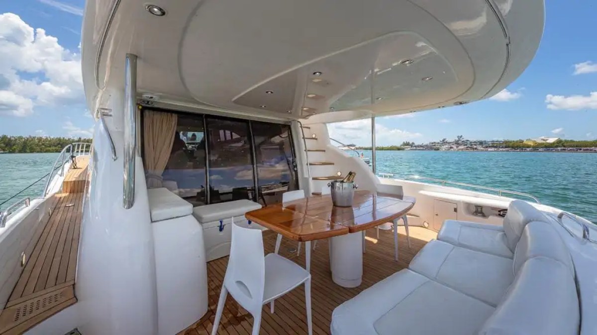 Luxury yacht deck with wooden table, white chairs, and sea view.