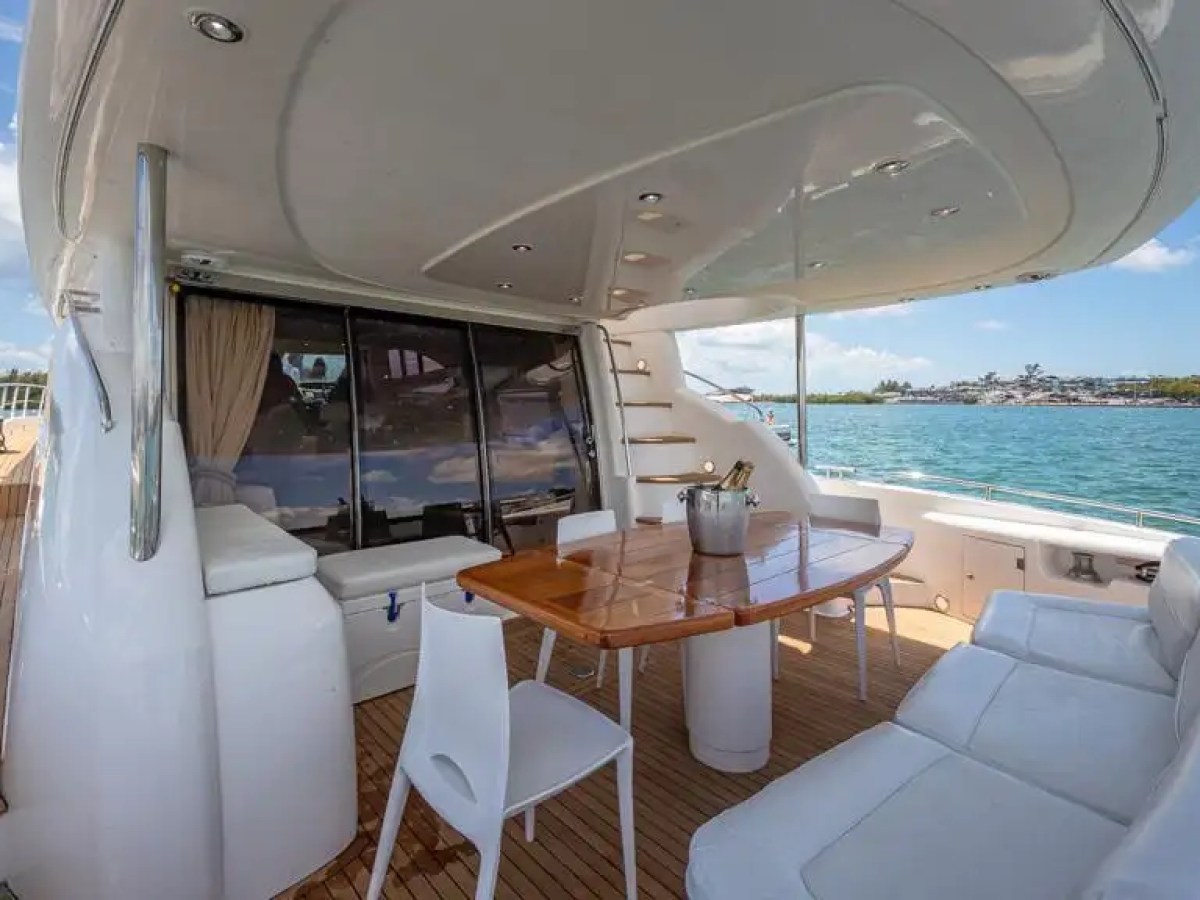 Luxury yacht deck with wooden table, white chairs, and sea view.