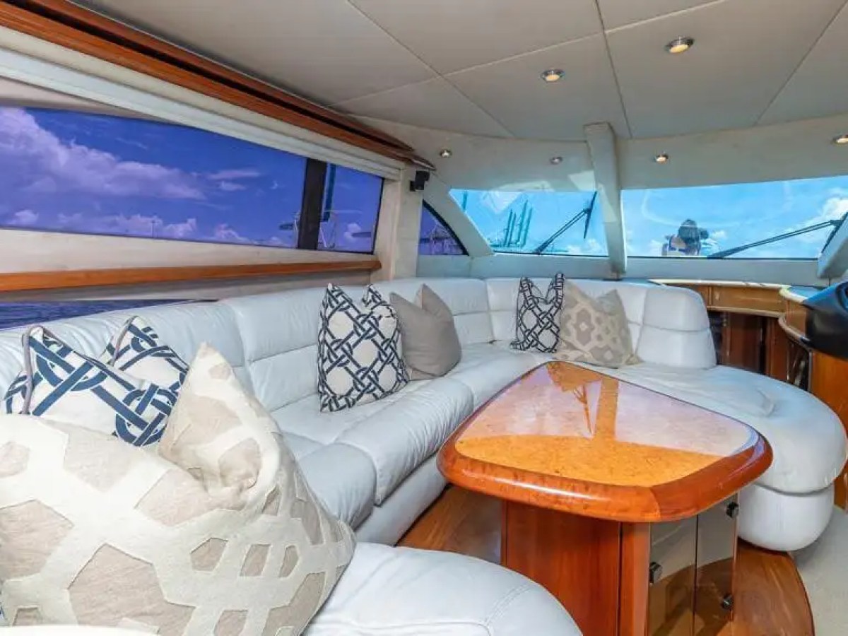 Luxurious yacht interior with white seating, pillows, and wood table under a blue sky view.