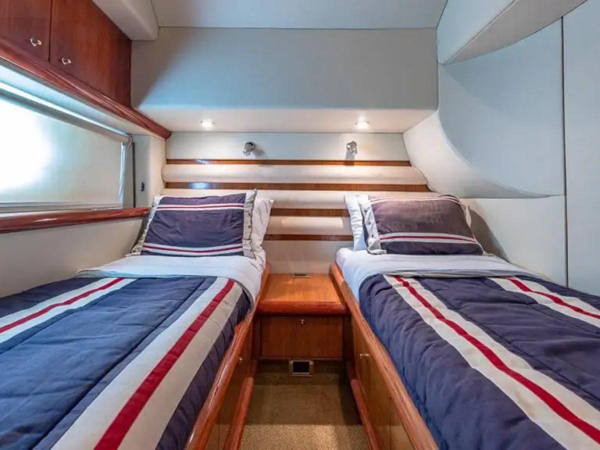 Small cabin with two twin beds, blue and red striped bedding, wood cabinets, and overhead lighting.