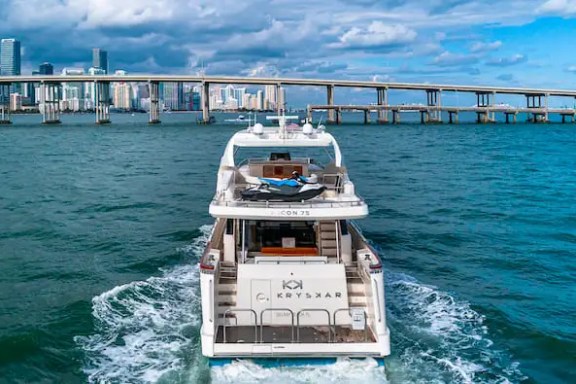 Yacht on water near city skyline and bridge under a cloudy sky.