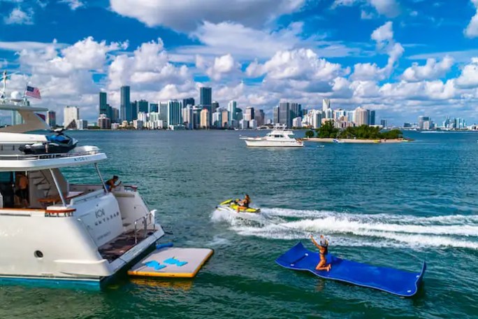 Yacht and jet ski in ocean with city skyline and clouds in background.