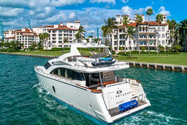 Luxury yacht on water near waterfront condos and palm trees under a blue sky.