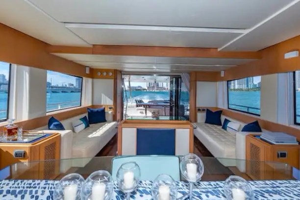 Luxurious yacht interior with large windows, beige seating, blue cushions, and a view of the sea.