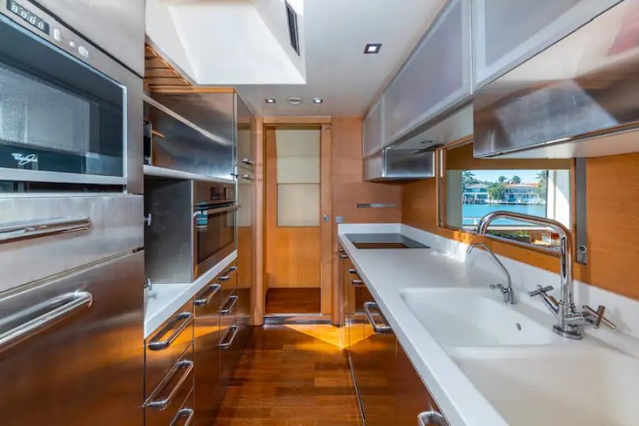 Modern narrow kitchen with stainless steel appliances, wooden floor, and large sink by a window.