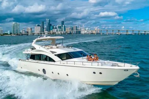 A yacht cruising near a city skyline with a bridge in the background and people relaxing on deck.