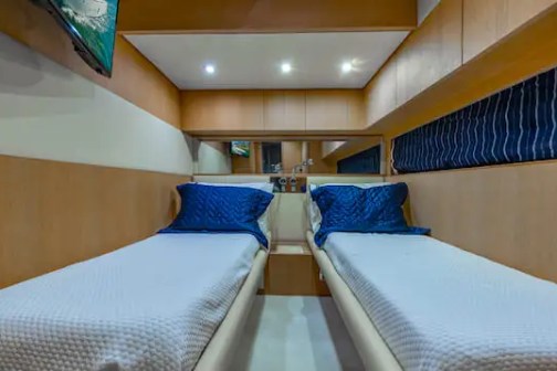 Small bedroom with two narrow beds, blue pillows, and white bedspreads.