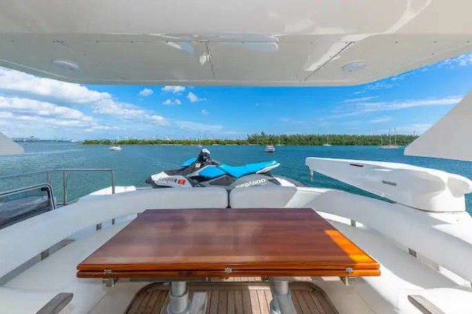 View from a yacht's cabin with a wooden table, jet ski on the deck, and ocean view.