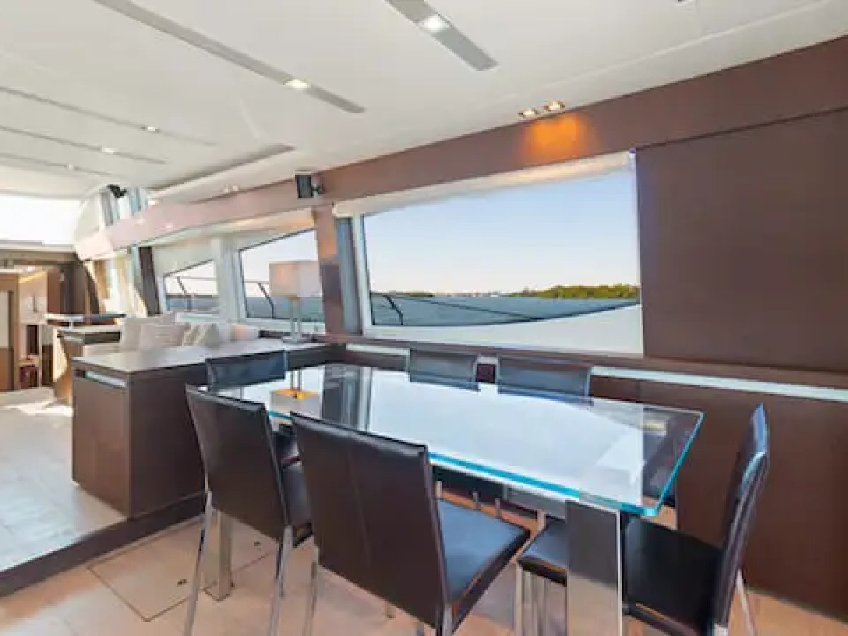 Modern yacht interior with glass dining table and six chairs, large windows, and view of the sea.
